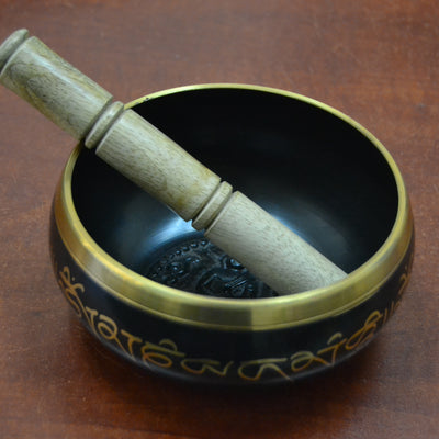 Close-up of a Tibetan brass singing bowl paired with a wooden mallet resting on the rim, showcasing its intricate design and golden details.