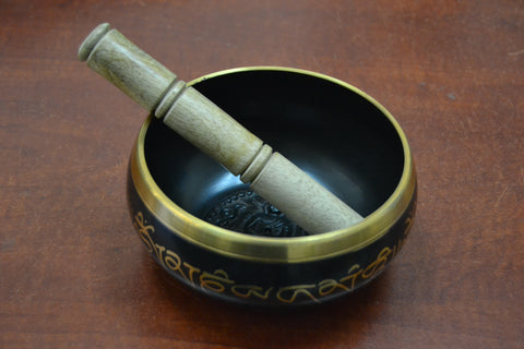 Close-up of a Tibetan brass singing bowl paired with a wooden mallet resting on the rim, showcasing its intricate design and golden details.