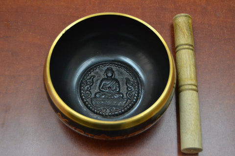 Interior view of the brass singing bowl, featuring an engraved Buddha design at the bottom and the wooden mallet placed beside it.