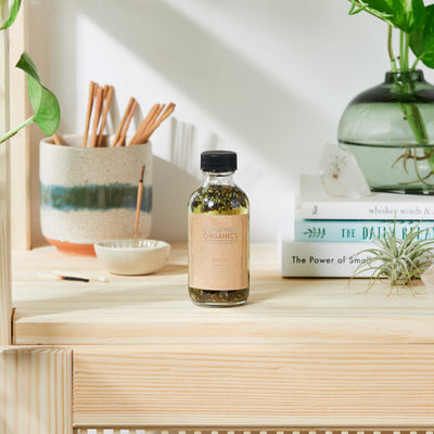 Bottle of Lavender Bath Oil displayed on a wooden shelf with books and plants.