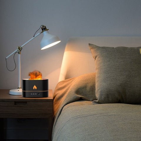 Black flame diffuser placed on a nightstand next to a bed and lamp.