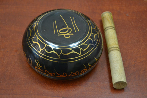 Brass singing bowl turned upside down, highlighting the intricate golden engravings on its exterior, with a wooden mallet placed beside it.